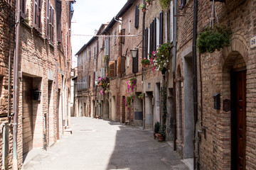 Fototapeta na wymiar Narrow street of a village of umbria and tuscany, with wooden doors and flower pots on the walls of facades of ancient brick houses