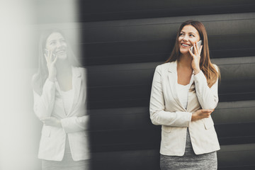 Pretty businesswoman with mobile phone in front of office building