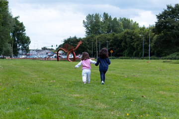 Fototapeta premium Two little girls walking away in the grass in a park facing away from the camera
