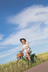 Beautiful young woman riding bicycle in a field
