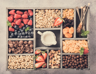 Variety of cold quick breakfast cereals with berries in old gray wooden box and other ingredients for breakfast, healthy eating concept, top view. Retro style toned.