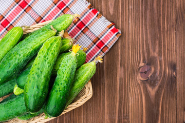 Fresh cucumbers in a basket on the napkin on a wooden table. Top view