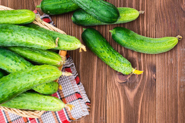 Fresh cucumbers in a basket and on a wooden table. Top view