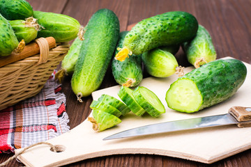 Sliced cucumber on a cutting board, knife and cucumbers in the basket and on a wooden table