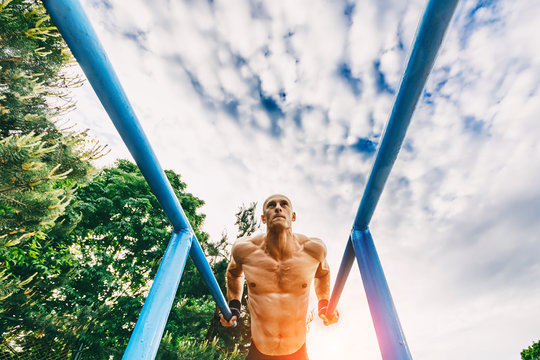 Bald Man doing push ups on parallel bars in a park