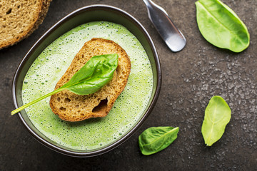 Homemade spinach soup puree in a dark bowl on a dark background with grain bread. Top View.