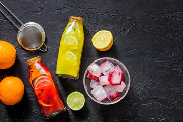 Bottle of fresh lemonade, fruits and ice cubes on black stone background top view copyspace