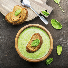 Homemade spinach soup puree in a dark bowl on a dark background with grain bread. Top View.
