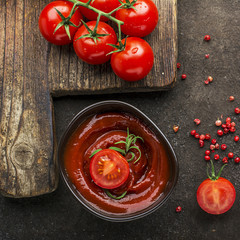 Dark ceramic bowl with tomato sauce, fresh vegetables, herbs, pepper on a dark background. Top View.
