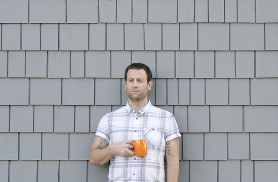 Millennial man holding a coffee mug with a grey neutral background.