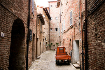 Obraz premium Alleyway of a medieval village with a red typical Italian country car in Italy.