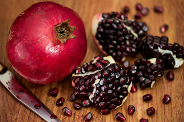A pomegranate on a wooden table with some  morsels and a knife
