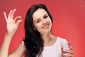 Beautiful young woman on a red background holds a pill