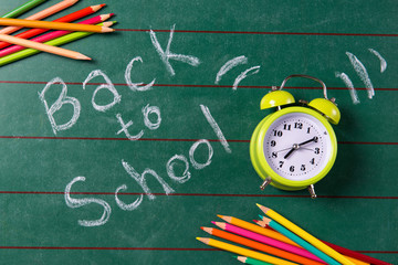 Alarm clock and colored pencils on the chalkboard with back to school text, top view