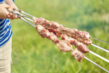 The middle aged woman hands with pieces of meat for a shish kebab barbeque on skewers with green blurry background