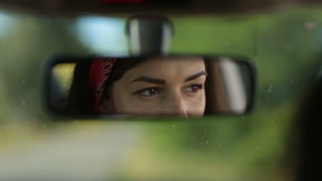 Reflection of cute woman in car rearview mirror