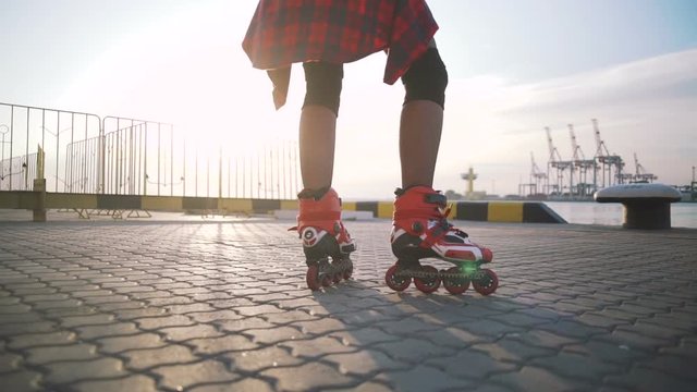 Young stylish funky girl with green hair riding roller skates and dancing near sea port during sunset, slow motion