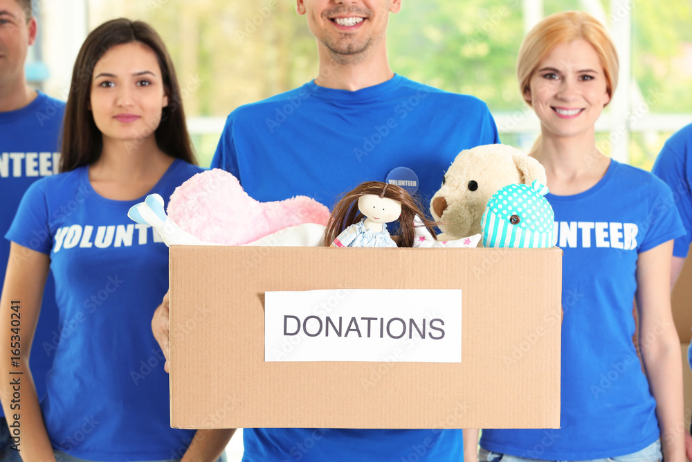 Wall mural Young volunteers with box of donations indoors