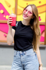 Outdoor portrait of young attractive woman with long blonde straight hair, pink glasses, pink lipstick and berry's smoothie cocktail, colorful background. Healthy food detox concept