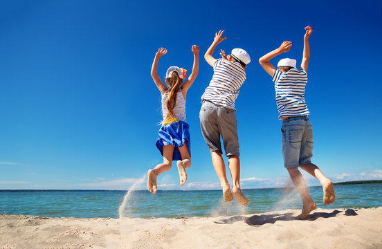 children jumping on the beach in summer hats. Boys and girl having fun at seaside