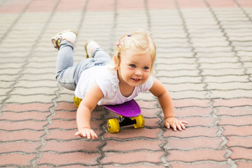 A small blonde girl lies on a skateboard. Repels his hands when riding.