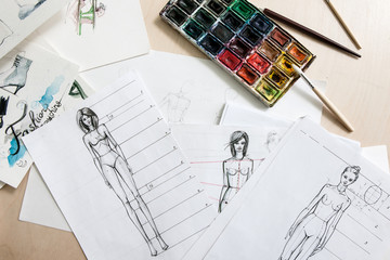 Designer fashion sketches of models with watercolor paint on desk
