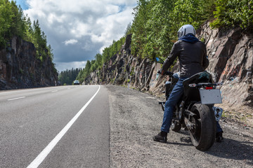 Man with modern naked motorcycle standing on roadside of the mountain asphalt road, rear view,...
