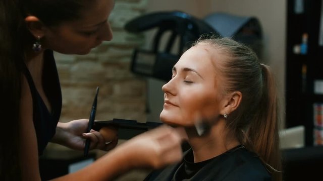 Structuring procedure.Make-up artist puts foundation on the face of the young woman.Make-up artist with a brush for the face makes the makeup girl.Makeup. Cosmetic. Base for Perfect Make-up.Applying