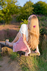 ein blondes Mädchen auf einer Parkbank  hängt Ihre langen Haare nach hinten in die Abendsonne