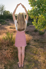 hübsches, blondes Mädchen von hinten umrahmt mit den Armen die Abendsonne  in der Natur bei...