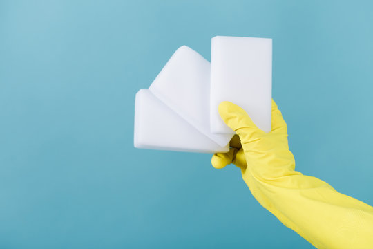 hand  in a rubber yellow glove holding sponge on blue background.