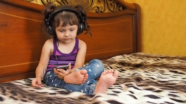 Child with mobile phone. A little girl in headphones with a mobile phone is listening to music.