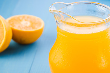 glass jug of yellow juice and orange fruit on a blue background/glass jug of yellow juice and orange fruit