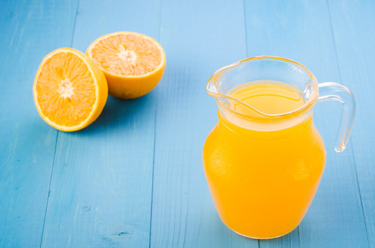 glass jug of yellow juice and orange fruit on a blue table/glass jug of yellow juice and orange fruit on a blue background
