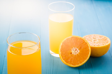 two glass of yellow juice and orange fruit/two glass of yellow juice and orange on a blue background