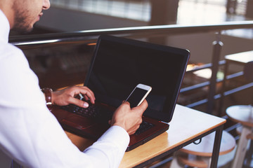 Young man working using smart phone and notebook computer, man's hands using smart phone in interior, man at his workplace using technology, close up