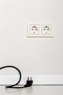 Black power cord cable unplugged with european wall outlet on white plaster wall