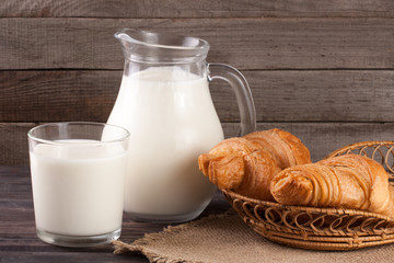 jug and glass of milk with croissants on a wooden background