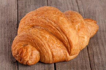 one croissant on old wooden board closeup