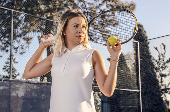 Portrait of beautiful female tennis player holding racket behind her back , outdoors, sunset 