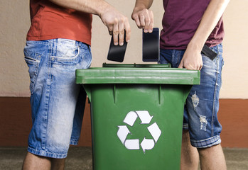 Two unrecognizable man throwing smartphones in recycle bin , outdated, obsolete technology 