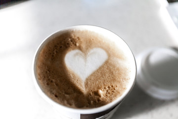 Coffee latte in a plastic mug, artistic heart pattern on top