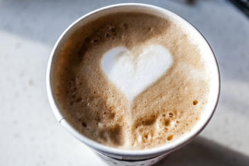 Coffee latte in a plastic mug, artistic heart pattern on top