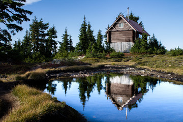 cabin on a mountain reflecting in an alpine lake