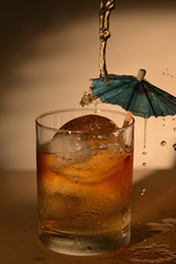 Liquor being poured over a paper umbrella in  a drink glass with an uce ball