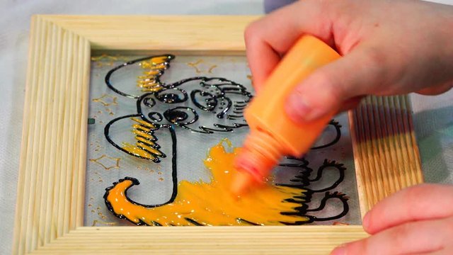 Orange paint from a tube pours a picture on the glass in a frame