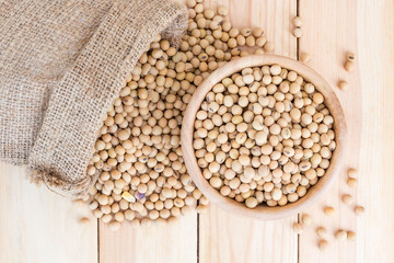 Fototapeta premium Soy beans in a wooden bowl and in sack on wooden background, Top view