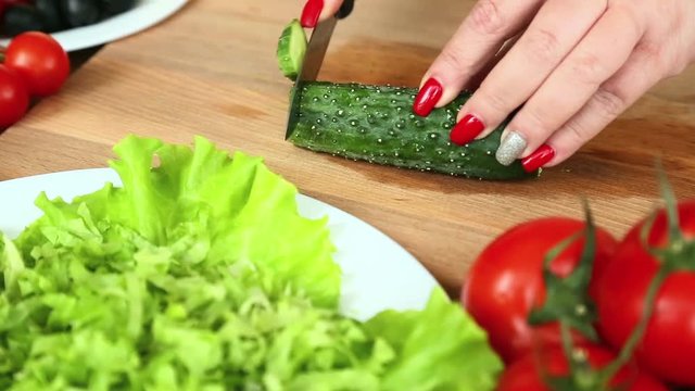 Preparation of homemade vegetable salad with cherry tomatoes, cheese and quail eggs. Female hands cut a cucumber with a knife. Camera moves from right to left