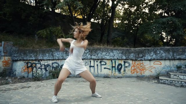 Young Asian woman dancing modern choreography in city park, outside. City ruins and graffiti. With elements of jazz, funk, hip-hop.