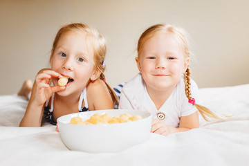 Portrait of two white Caucasian children girls eating corn puffs. Sisters eating snack fast food in...